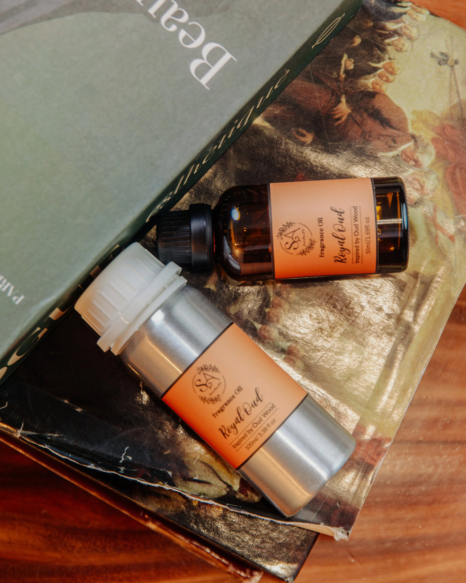 Two bottles of 'Royal Oud' fragrance diffuser oil on a textured surface with a book in the background.