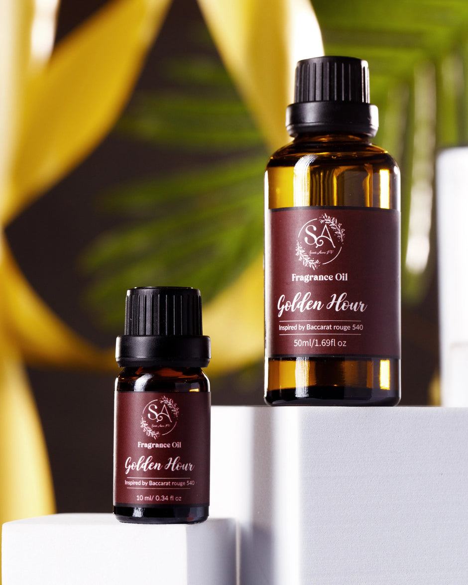 Two bottles of 'Golden Hour' fragrance oil on a white surface with a blurred green leafy background.
