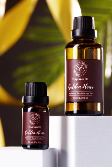 Two bottles of 'Golden Hour' fragrance oil on a white surface with a blurred green leafy background.