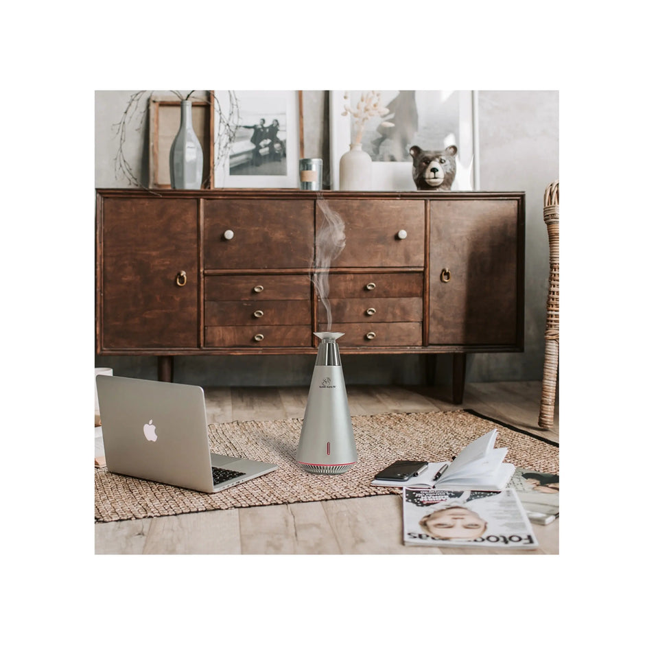 Laptop on a wooden floor with a diffuser emitting steam, a dresser in the background.