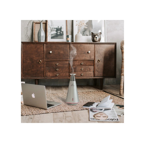 Laptop on a wooden floor with a diffuser emitting steam, a dresser in the background.