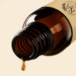 Brown glass bottle with black cap and diffuser oil dripping, beige background